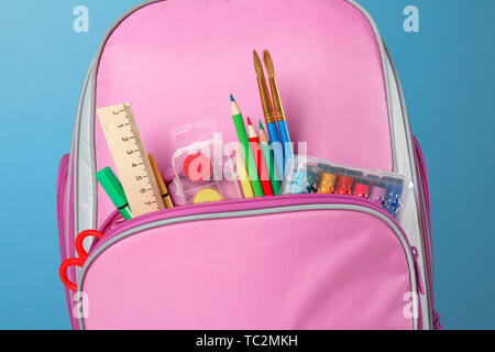 Nahaufnahme von rosa Rucksack mit Büromaterial vor einem blauen Hintergrund. Zurück zu Schule. Der Begriff der Bildung. Stockfoto
