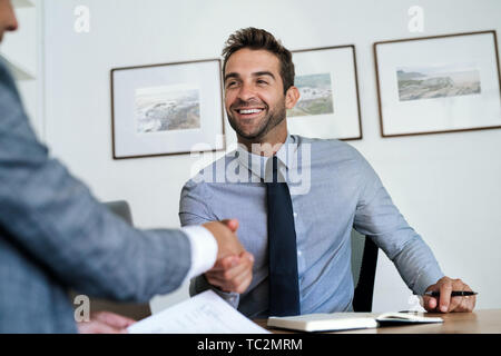 Manager an seinem Schreibtisch Händeschütteln mit einem Mitarbeiter sitzen Stockfoto