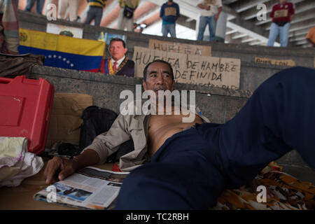 04. Juni 2019, Venezuela, Caracas: ein Mann liegt vor der Venezuelanischen Flagge und ein Porträt der späten Staatschef Hugo Chavez in einem Protest, in dem ehemaligen Arbeitnehmer, die Aufmerksamkeit auf sich mit einem Hungerstreik zu zeichnen möchten. Einige Männer haben im Hungerstreik für sechs Tage. Ehemalige Exxon Mobil Oil Company Arbeiter fordern Zahlung von Vereinbarungen und Sozialversicherungsbeiträge hervorragende Nach der Verstaatlichung von US Oil Company Projekt in Venezuela. "Präsident Maduro und seine Minister wird sicherlich drei Mahlzeiten am Tag in Ruhe essen. Er sollte auch denken, der uns [.] und unserer Stockfoto