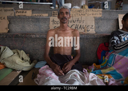 04. Juni 2019, Venezuela, Caracas: "Wir sind Arbeiter und im Streik", auf Karton hinter einem Mann, der zusammen mit einer Gruppe von ehemaligen Arbeitnehmern, zieht Aufmerksamkeit mit einem Hungerstreik geschrieben. Einige Männer haben im Hungerstreik für sechs Tage. Ehemalige Exxon Mobil Oil Company Arbeiter fordern Zahlung von Vereinbarungen und Sozialversicherungsbeiträge hervorragende Nach der Verstaatlichung von US Oil Company Projekt in Venezuela. "Präsident Maduro und seine Minister wird sicherlich drei Mahlzeiten am Tag in Ruhe essen. Er auch an uns denken [.], unserer legitimen Forderung sollten", sagt 60 Stockfoto