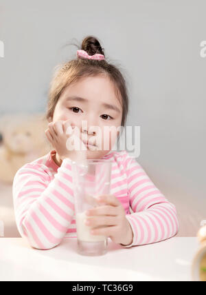 Das kleine Mädchen trinken Milch und den Wecker auf dem Tisch. Stockfoto