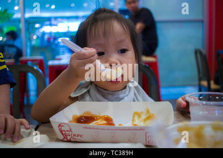 CHIANGMAI, THAILAND - Mai 3,2019: Kleines Kind essen gebratenes Huhn in den Hintergrund des KFC-Restaurant. Stockfoto