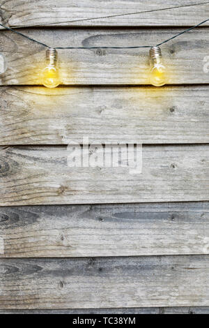 Outdoor-String Lichter hängen auf Linie Kindheit in einem Garten im Hinterhof. Grungy verwitterte Holzbretter Hintergrund Textur Stockfoto