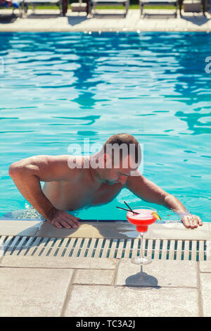 Der Mann schwimmte im Schwimmbad im Urlaub in Italien. Der Mann kommt aus dem Swimmingpool, um einen Ananascocktail zu trinken Stockfoto