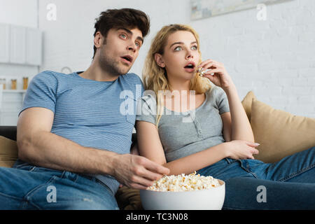 Schockiert Mann ansehen Film in der Nähe von blondes Mädchen und Schüssel mit Popcorn Stockfoto