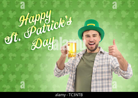 Hübscher junger Mann im grünen Hut und mit Becher Bier mit Daumen-nach-oben-Geste gegen Farbe Hintergrund. St. Patrick's Day Celebration Stockfoto