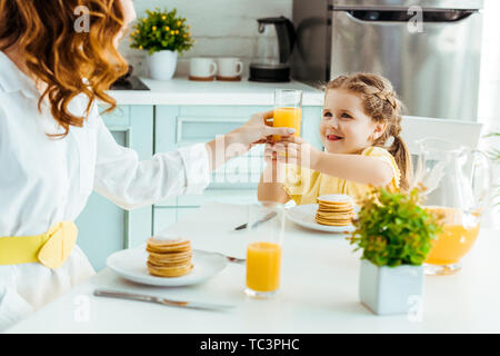 Selektiver Fokus der Mutter, Glas mit Orangensaft zu lächeln Tochter beim Frühstück Stockfoto