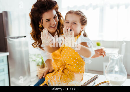 Lächelnde Mutter zu lachen Tochter mit schmutzigen Händen im Teig suchen Stockfoto
