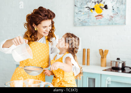 Selektiver Fokus der glücklichen Mutter und Tochter sieben Mehl zusammen in der Küche Stockfoto