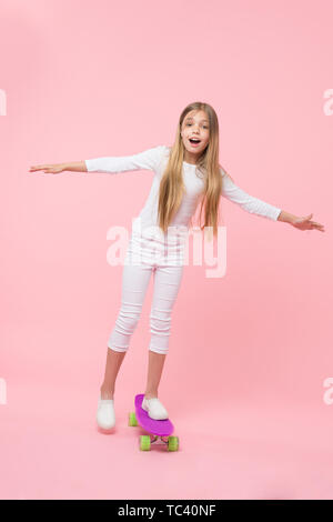 Regenerieren ihre Energie skateboarding. Adorable kleine Kind durchführen skateboarding Tricks auf rosa Hintergrund. Kleines Mädchen skateboarding auf Violett penny board Niedlich. Go skateboarding Day. Stockfoto