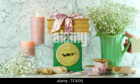 Vintage Küchenwaage Dekor Einstellung mit Porzellan Kanne gypsophila Blumen, Kerzen, Blumen Bänder und alte Bücher. Stockfoto