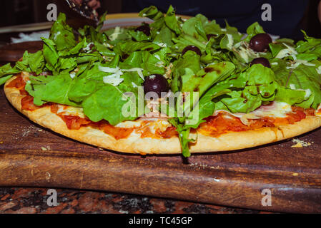 Lecker lecker Pizza mit Käse, Tomaten, Rucola, Oliven, Basilikum auf hölzernen Tisch Stockfoto
