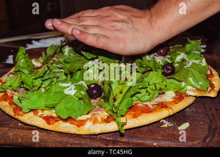 Lecker lecker Pizza mit Käse, Tomaten, Rucola, Oliven, Basilikum auf hölzernen Tisch Stockfoto