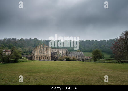 Dunkle Wolken hängen über dem 11. Jahrhundert Ruinen von Rievaulx Abbey, eine von Englands größtem Zisterzienserklöster, in der North York Moors Stockfoto
