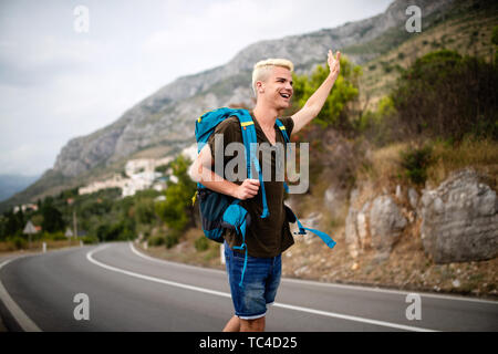 Per Anhalter, junge Reisende Mann versuchen Auto auf einer Forststraße zu fangen Stockfoto