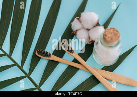 Meersalz in Glasflasche, natürliche Zahnbürsten und Baumwolle Blume auf palm leaf blauen Hintergrund. Stockfoto