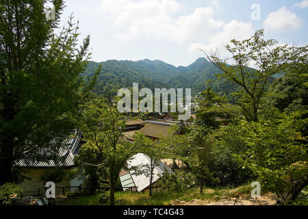 Dächer japanische Häuser" Gesehen von oben, mit grünen, bewaldeten Bergen im Hintergrund, auf der Insel Miyajima, Hiroshima, Japan. Stockfoto