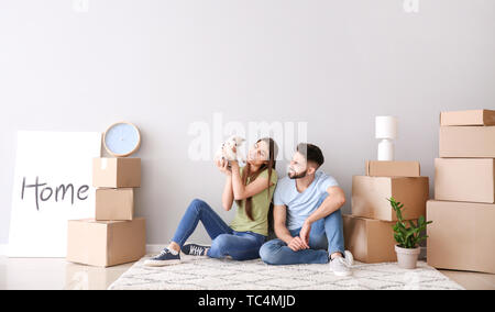 Junges Paar mit Sachen und Kätzchen saß in der Nähe von hellen Wand in Ihrem neuen Haus Stockfoto