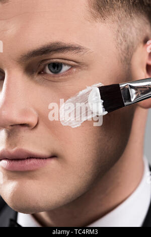 Nahaufnahme Sicht des Menschen Anwendung Creme im Gesicht mit kosmetischen Bürste Stockfoto
