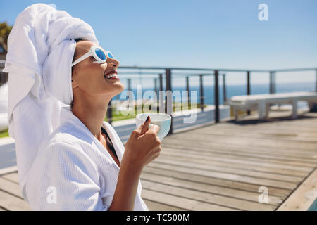 Fröhliche Frau im Bademantel an der Poolbar mit einer Tasse Kaffee. Lächelnd kaukasischen Frauen Kaffee nach dem Schwimmen. Stockfoto