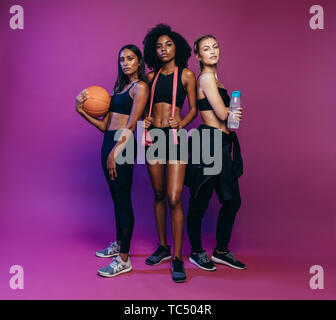 Gruppe von weiblichen Freunde in Sportkleidung gemeinsam auf farbigem Hintergrund. Drei Frauen an der Turnhalle Klasse mit Basketball, Resistance Band und ein Wasser Stockfoto