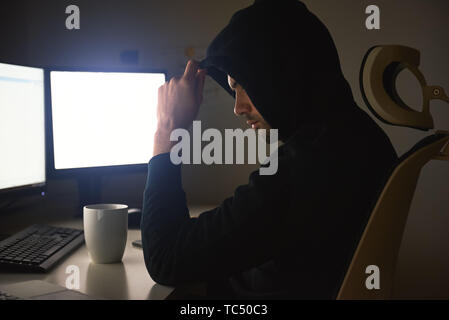 Computer Hacker. Junge Mann in Schwarz hoodie mit mehreren Computern für das Diebstahl von Daten während der Sitzung in dunklen Zimmer. Der binäre Code. Cyber Attack. Cyber Security Stockfoto