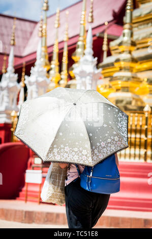 Eine Thailänderin hält einen Regenschirm auf, um sich vor der Sonne im Wat Phra Sing Temple, Chiang Mai, Thailand zu schützen. Stockfoto