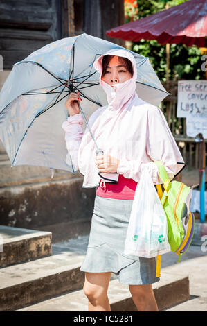 Eine asiatische Tourist blendet sich aus der rauen Sonne mit Regenschirm im Wat Phant Tao Tempel in Chiang Mai, Thailand. Stockfoto