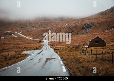Bild von Reisen auf einer einsamen Straße in den Färöer Inseln. Berge und traditionellen Häusern. Stockfoto