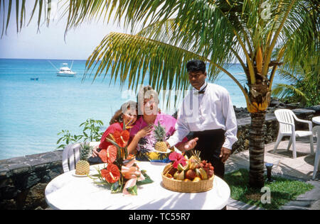 Der Sänger Klaus Baumgart posiert im Urlaub vermutlich auf den Bahamas im Außenbereich des Hotels mit seiner Ehefrau Ilona Schulz-Baumgart unter Palmen mit einem üppigen Obstkorb, Ca. 1970er. Der Sänger Klaus Baumgart stellt auf Ferien wahrscheinlich auf den Bahamas im Außenbereich des Hotels mit seiner Frau Ilona Schulz-Baumgart unter Palmen mit einem üppigen Obstkorb, ca. 1970er-Jahre. Stockfoto