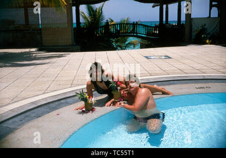 Der Sänger Klaus Baumgart posiert im Urlaub vermutlich auf den Bahamas Hotelpool mit seiner Ehefrau Ilona Schulz-Baumgart 5/6 sie Cocktails und frisches Obst genießen, Ca. 1970er. Der Sänger Klaus Baumgart stellt wahrscheinlich Urlaub auf den Bahamas Hotel Pool mit seiner Frau Ilona Schulz-Baumgart, während Sie Cocktails und frischem Obst, um 1970 n. Stockfoto