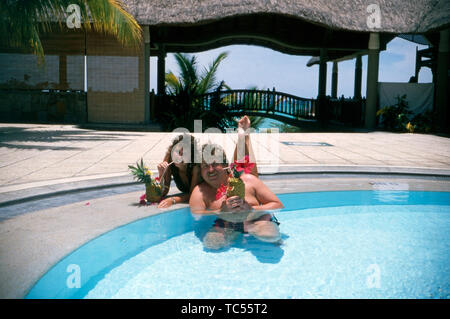 Der Sänger Klaus Baumgart posiert im Urlaub vermutlich auf den Bahamas Hotelpool mit seiner Ehefrau Ilona Schulz-Baumgart 5/6 sie Cocktails und frisches Obst genießen, Ca. 1970er. Der Sänger Klaus Baumgart stellt wahrscheinlich Urlaub auf den Bahamas Hotel Pool mit seiner Frau Ilona Schulz-Baumgart, während Sie Cocktails und frischem Obst, um 1970 n. Stockfoto