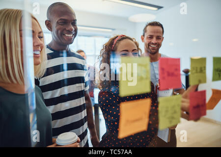 Team von lächelnden Designer gemeinsam in einem Büro Brainstorming mit Haftnotizen auf eine Glaswand Stockfoto
