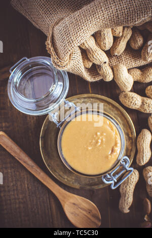 Erdnussbutter im Glas Glas mit Erdnüsse in der Schale auf Holz- Hintergrund. Vegetarisches Essen Konzept. Stockfoto