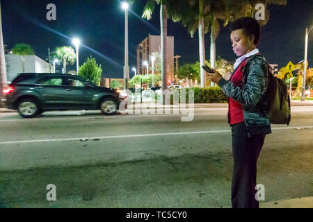 Miami Beach Florida, North Beach, Collins Avenue, Schwarze Schwarze Afrikaner ethnische Minderheit, Erwachsene Erwachsene Frau Frauen weibliche Dame, Bushaltestelle, Nacht, Readi Stockfoto