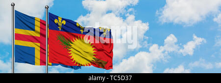 Aland Inseln und Guadeloupe Flagge im Wind gegen Weiße bewölkt blauer Himmel zusammen. Diplomatie Konzept, internationale Beziehungen. Stockfoto