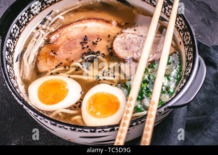 Udon Nudeln in japanische Ramen Suppe mit Schweinefleisch, Eier und Schalotten auf dunklem Hintergrund Stockfoto