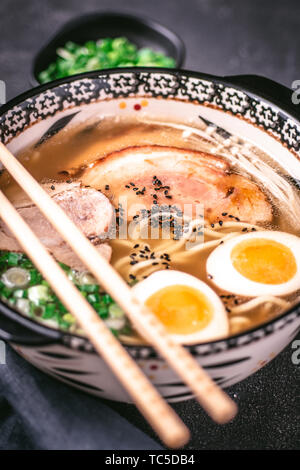 Udon Nudeln in japanische Ramen Suppe mit Schweinefleisch, Eier und Schalotten auf dunklem Hintergrund Stockfoto