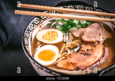 Udon Nudeln in japanische Ramen Suppe mit Schweinefleisch, Eier und Schalotten auf dunklem Hintergrund Stockfoto