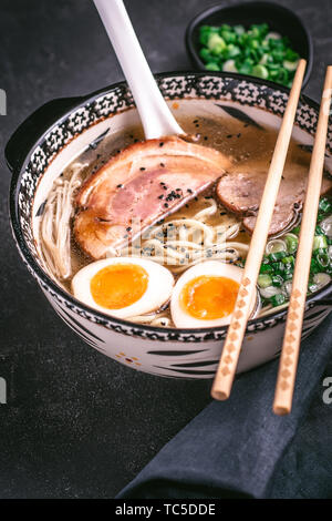 Udon Nudeln in japanische Ramen Suppe mit Schweinefleisch, Eier und Schalotten auf dunklem Hintergrund Stockfoto