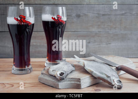 Auf einer hölzernen Tisch zwei Gläser Bier, neben dem Schneidebrett getrockneten Fisch und ein Messer. Stockfoto