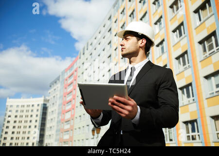 Low Angle Portrait von Stattlichen des Nahen Ostens Geschäftsmann, tragen, hardhat stehend gegen Wohnanlage auf Baustelle, kopieren Raum Stockfoto