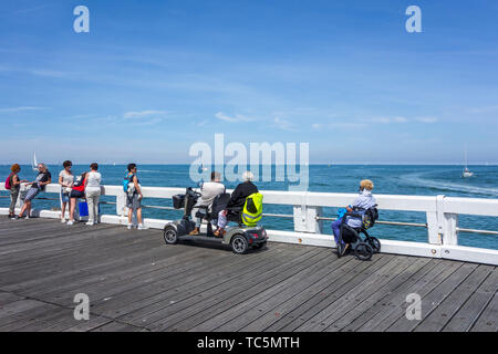 Behinderte Frau im Rollstuhl und Behinderte im Duo zwei Person scooterverleih Segelboote beobachten auf See von Jetty Stockfoto