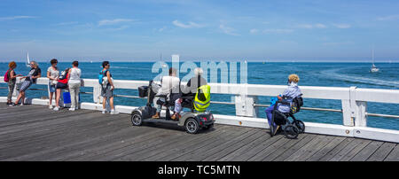 Behinderte Frau im Rollstuhl und Behinderte im Duo zwei Person scooterverleih Segelboote beobachten auf See von Jetty Stockfoto