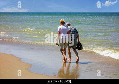 Ältere Paare Paddeln im flachen Wasser am Sandstrand entlang der Küste im Sommer Stockfoto