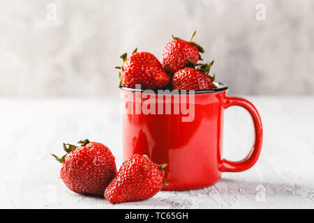 Frische Erdbeeren in rot Emaille Tasse auf grauem Hintergrund Stockfoto