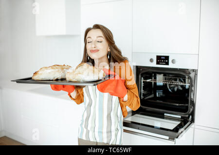 Porträt einer wunderschönen jungen Frau Brot backen im Ofen bei der Moderne, weiße Küche zu Hause Stockfoto