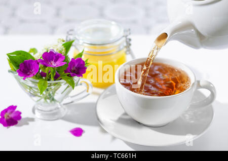 Heiße Tasse Tee mit Minze und Honig auf weißem Hintergrund. Der Prozess der gießen Tee. Selektive konzentrieren. Stockfoto