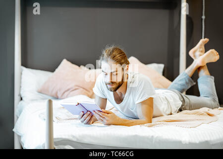 Schöner Mann im Pyjama Buch zu lesen, während sie sich auf dem Bett zu Hause. Stockfoto