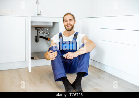 Porträt von einem gutaussehenden Klempner in Overalls in der Nähe der Spüle in der Küche sitzt Stockfoto